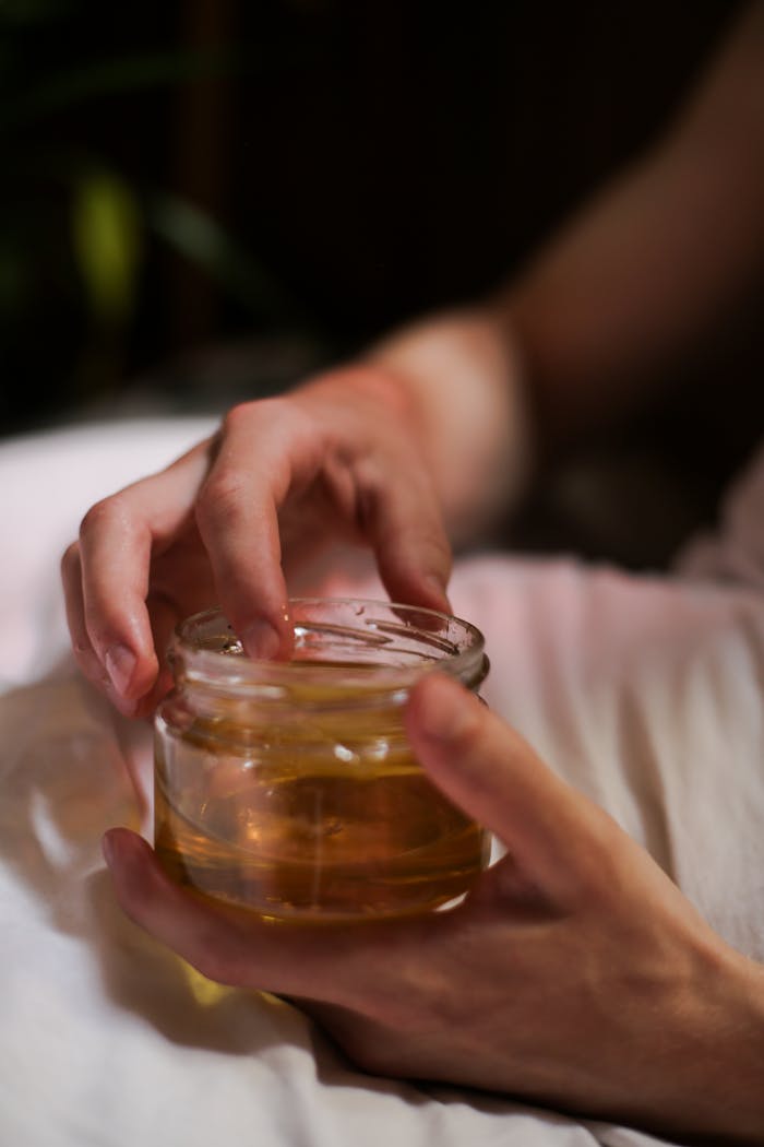 gallery-5 Close-up of a person's hands holding a glass jar filled with honey. Indoors scene with soft lighting.